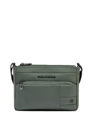 Kleine groene crossbodytas met voorvak met ritssluiting, verstelbare zwarte band en een reliëflogo op een glad oppervlak.
