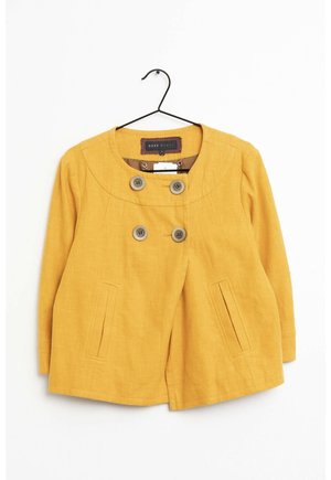 Yellow women's jacket with round collar and four large buttons, displayed hanging on a black metal hanger against a white background.