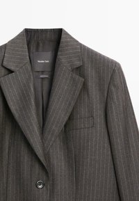 Grijze pinstripe blazer van gestructureerde stof, met notch-revers, een enkele knoopsluiting en een borstzak met een label aan de binnenkant.