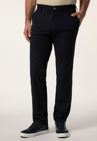 Mörkblå bomullbyxor med slim fit, framfickor och en knappstängning, kombinerat med mörka sneakers för en avslappnad look.