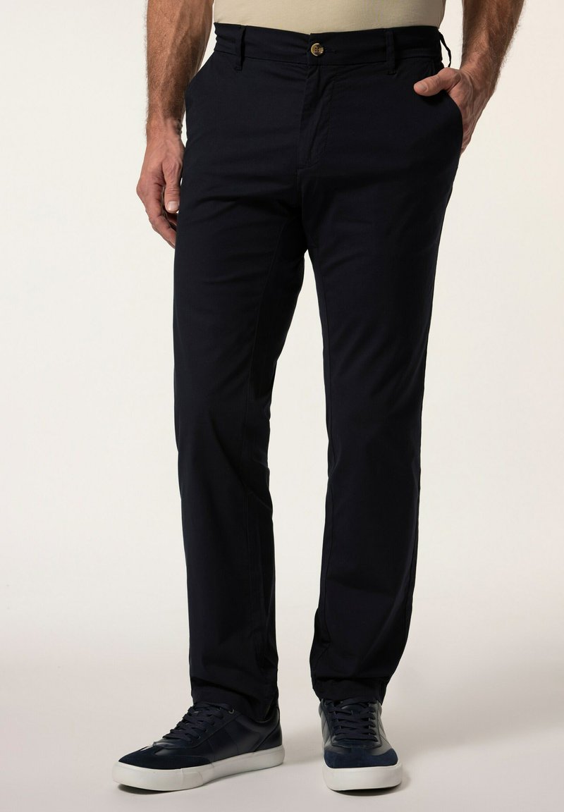 Mörkblå bomullbyxor med slim fit, framfickor och en knappstängning, kombinerat med mörka sneakers för en avslappnad look.