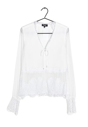 Witte blouse met lange mouwen en kanten afwerking aan de manchetten en zoom, V-hals met strikdetail, hangend aan een zwarte hanger tegen een witte achtergrond.