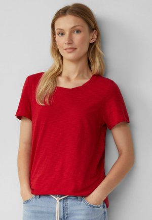 Rotes Kurzarm-T-Shirt mit rundem Halsausschnitt und strukturiertem Stoff, kombiniert mit hellblauen Jogginghosen mit Kordelzug.