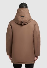 Braune isolierte Jacke mit hohem Kragen und verstellbarem Kapuzen. Sie hat einen glatten Stoff, seitliche Schlitze am Saum und ein minimalistisches Design.
