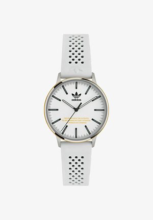 Balta laikrodis su silikoniniu dirželiu, turinčiu perforuotą dizainą, sidabrinis nerūdijančio plieno korpusas ir baltas ciferblatas su juodais valandos žymekliais. Aukso tekstas ciferblate.