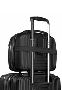 Zwart hardshell bagage gestapeld, met een gestructureerd oppervlak, stevige metalen handgreep en een riem die de bovenste koffer beveiligt.
