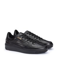 Le sneakers in pelle nera presentano una superficie liscia, una punta perforata, una spessa suola in gomma e lacci neri. Il marchio dorato è visibile sul lato.