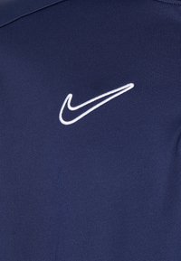 Marineblaue Sportshirt mit einem weißen, gestickten Nike-Logo auf der linken Brust, aus einem glatten, strukturierten Stoff gefertigt.