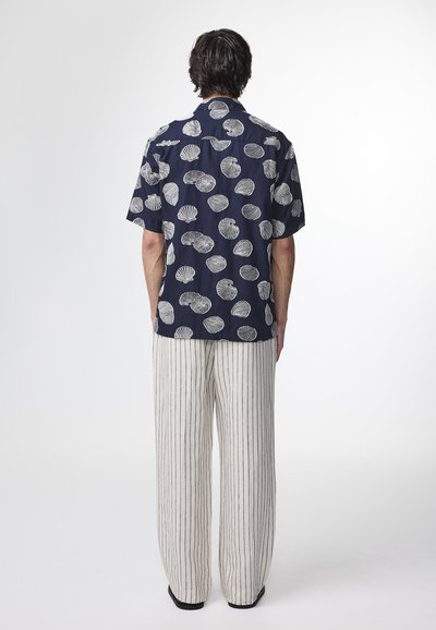 Camicetta a maniche corte di colore blu navy con motivo a guscio bianco, abbinata a pantaloni a righe beige chiaro, con texture visibile in entrambi i materiali.