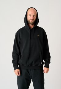 Black hooded sweatshirt made of cotton blend, featuring a front pocket and embroidered logo in yellow on the chest. Casual fit with ribbed cuffs.