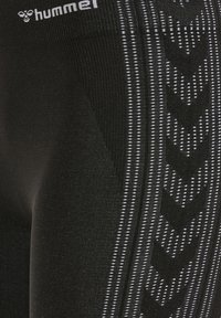 Schwarze Sportleggings mit weißen Chevron-Musterstreifen an der Seite und „hummel“-Logo am Bund.