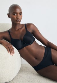 Black seamless bra with molded cups and adjustable straps, paired with matching briefs featuring a textured trim. Soft fabric, minimalist design.