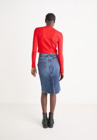 Czerwony prążkowany top z długim rękawem w połączeniu z ołówkową spódnicą dżinsową z wysokim stanem. Czarne botki za kostkę dopełniają całość.