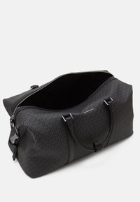 Sac de sport noir avec un motif de logo, deux poignées et une fermeture éclair. Dispose d'un intérieur spacieux et d'une texture lisse. Accents en métal argenté.