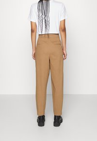 Pantalon marron taille haute avec une coupe ajustée, doté de deux poches arrière et d'une texture lisse, associé à une chemise blanche à manches courtes.