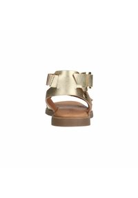 Metalen gouden sandalen met twee verstelbare gespen. Het open achterkantontwerp, de platte zool en de gladde leren textuur onderscheiden het schoeisel.