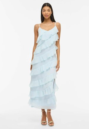 Robe maxi bleu clair avec volants superposés, fines bretelles et fente latérale. Fabriquée en tissu transparent avec un drapé fluide et une texture douce.