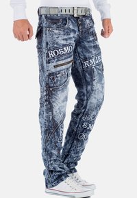 Pantaloni cargo in denim blu con effetto usurato, dotati di numerose tasche, dettagli con zip e branding ricamato in bianco. Presentano una finitura testurizzata e una vestibilità slim.