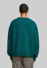 Tölgyzöld, oversized kötött pulóver kerek nyakkal és ejtett vállakkal, texturált anyagból készült, világos khaki cargo nadrággal párosítva.