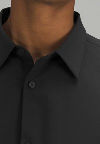 Camicia nera con colletto, caratterizzata da una texture liscia e opaca e due bottoni neri al collo. Design semplice e classico.