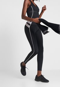 Czarny strój sportowy z topem na plecach i dopasowanymi legginsami. Posiada szare akcenty oraz logo Nike. W zestawie z czarnymi butami sportowymi.