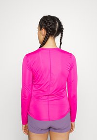 Langarmige, felroze sportshirt met een gladde, rekbare textuur, voorzien van een ronde halslijn en een subtiele naad langs de achterkant.