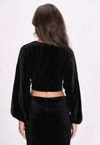 Schwarzes Samt-Crop-Top mit langen, puffigen Ärmeln und einem runden Ausschnitt, mit einem Rückverschluss und weichem, strukturiertem Stoff.