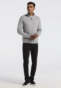 Grau Fleece-Pullover mit Reißverschlusskragen, gerippten Bündchen und Saum. Getragen mit schwarzen Slim-Fit-Hosen und schwarzen Sneakers mit weißen Sohlen.