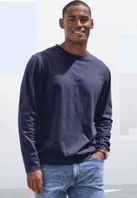 Marineblaue Langarmshirt aus weichem Stoff mit rundem Halsausschnitt, kombiniert mit hellblauen Jeans. Lässiger Schnitt mit minimalistischen Designdetails.