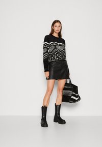 Maglione a righe bianche e nere con una consistenza pelosa, abbinato a una mini gonna in pelle nera e stivali neri chunky. Borsa a spalla nera e bianca.