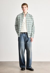 Grønn og hvit rutete skjorte over en kremfarget ribbestrikket tanktop, kombinert med løse blå denimjeans og svarte sko. Enkelt design og avslappet passform.