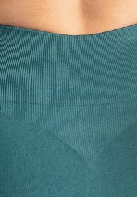 De teal geribbelde tailleband van de legging heeft een V-vormig ontwerp en een gladde textuur, met een gemengde stof voor comfort en ondersteuning.