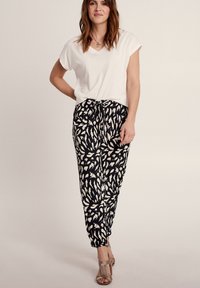 Witte korte mouwen V-hals t-shirt in combinatie met zwarte broek met een wit loofpatroon, en beige open teen hakken.