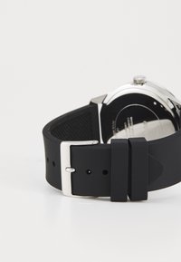 Correa de reloj de silicona negra con hebilla metálica plateada. Cuenta con un respaldo texturizado y múltiples agujeros de ajuste para un mejor calce. Diseño elegante.