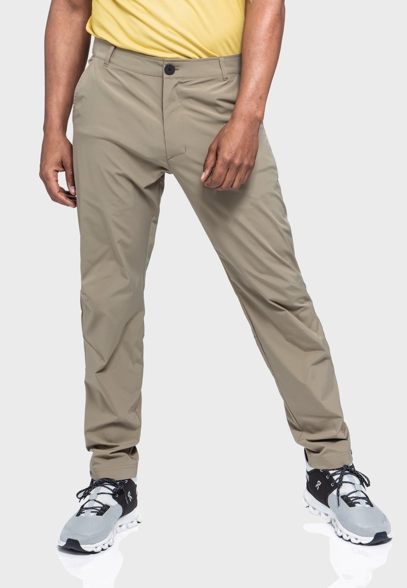 Beige, leichte, schlank geschnittene Hosen mit glatter Textur, Knopfverschluss und Fronttaschen. Kombiniert mit grauen Sportschuhen.