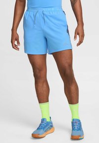 Blaue Sportschorts mit elastischem Bund, Kordelzug und seitlichen Einsätzen. Kombiniert mit blauen und orangen Schuhen sowie neon-grünen Socken.
