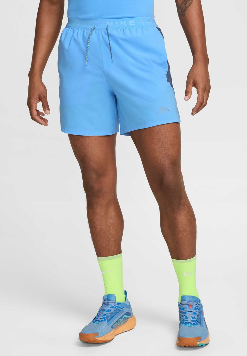 Blaue Sportschorts mit elastischem Bund, Kordelzug und seitlichen Einsätzen. Kombiniert mit blauen und orangen Schuhen sowie neon-grünen Socken.