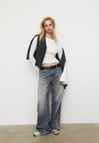 Grey wide-leg jeans paired with a fitted white top and a dark cardigan. Materials include denim, cotton, and knit. Silver sneakers complete the outfit.