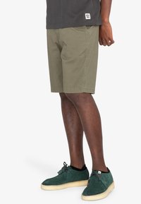 Gröna bomullsshorts för män med framfickor och en avslappnad passform, tillsammans med mörkgröna mockaskor och en grå t-shirt.