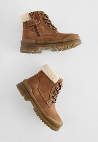 Bottines marron avec une bordure en fausse fourrure, fermeture à lacets à l'avant, zip sur le côté, semelle en caoutchouc et finition texturée, présentant un motif de semelle robuste.