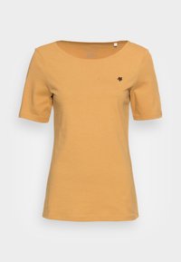 Koszulka z krótkim rękawem w kolorze musztardowym, wykonana z miękkiego materiału. Ma okrągły dekolt i małe czarne logo na lewej piersi.