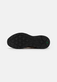 Semelle en caoutchouc noir avec des rainures profondes et des motifs hexagonaux. Présente le logo Timberland et un accent vert près du talon.