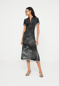 Μαύρο και γκρι φόρεμα με υφή, κοντά μανίκια, γιακά και κουμπωτό άνοιγμα· μήκος μέχρι τη μέση· συνδυασμένο με διαφανή γυαλιά ηλίου.