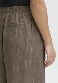 Bruna linbyxor med avslappnad passform, med en smockad midja och subtila metalltrådar som löper vertikalt, ficka sydd bak.