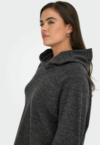 Siva kapuca s kapuco z teksturirano površino, ki ima širok ovratnik in sproščen kroj. Tkanina izgleda mehko in toplo.