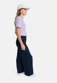Ljuslila T-shirt med korta ärmar och grafisk design; kombinerad med marinblå vidbyxor och vita sneakers; beige keps på huvudet.