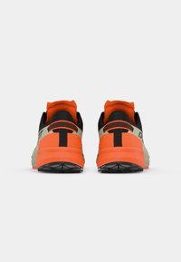 Πίσω όψη αθλητικών παπουτσιών με πράσινο και μαύρο άνω μέρος, φωτεινό πορτοκαλί τακούνι, υφασμάτινη σόλα και ζωηρές μαύρες λεπτομέρειες.