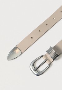 Ceinture en cuir beige avec une boucle ton argent poli, présentant une extrémité arrondie et plusieurs trous de réglage pour la taille.