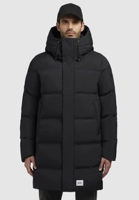 Sort puffervinterjakke med hætte, trykknapper og sidelommer. Tykt quiltet design med en struktureret overflade. Brandmærke synligt.