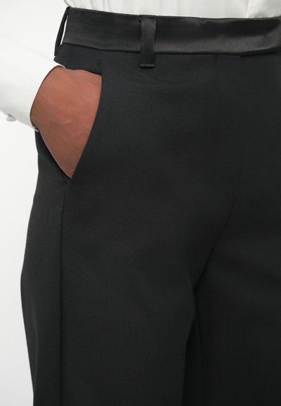 Musträbest jahid, mis on valmistatud tekstureeritud kangast, satiniga vöökoht ja küljetasku. Disain sisaldab kohandatud lõiget ja peeneid detaile.